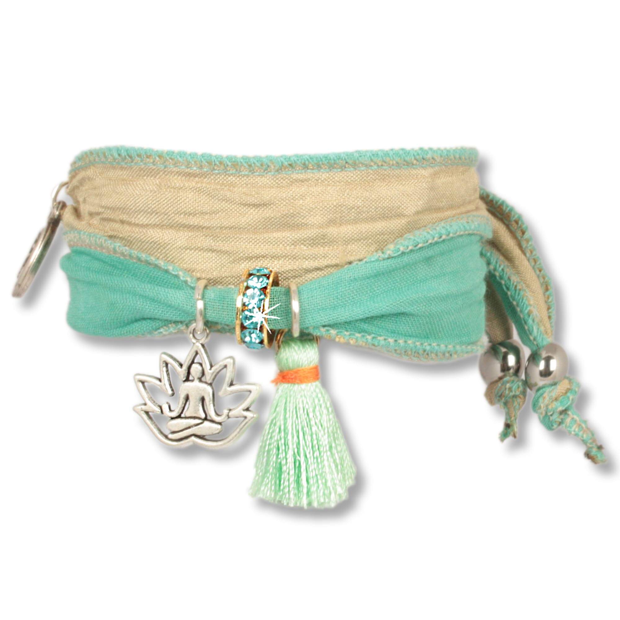 Handgefertigtes Stoffarmband aus Saris und Seidenstoffen in mint grün und Naturfarben. Verziert mit einer metallenen Lotusblume, die einen meditierenden Buddha zeigt, einer mintgrünen Seidenquaste, einem Rondell besetzt mit tschechischen Kristallen. Anísc
